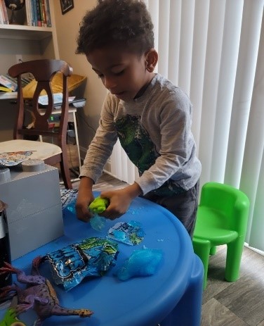 Winston is sitting next to a table and playing play-doh