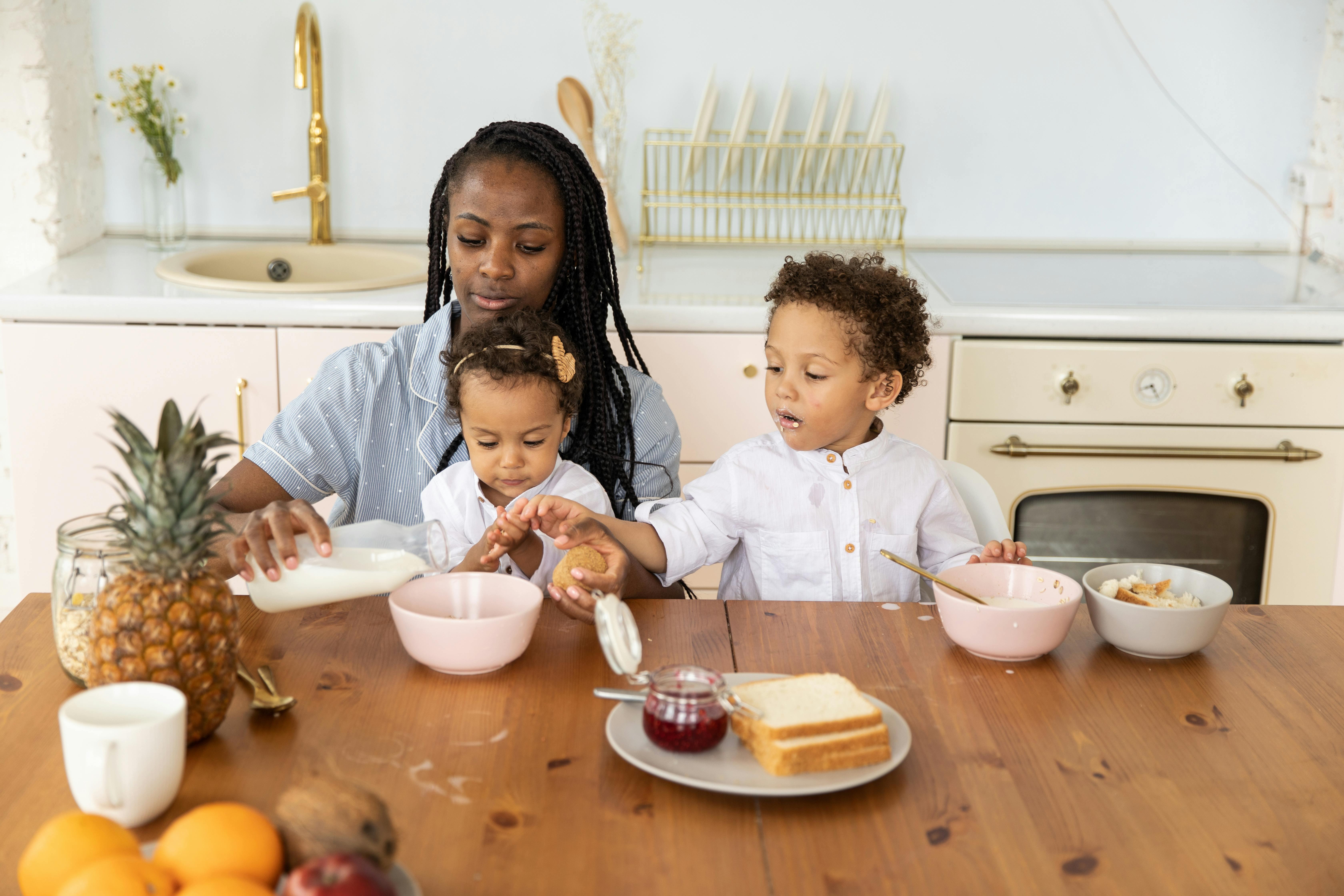 A mother and her two children enjoying breakfast together at a kitchen table.
