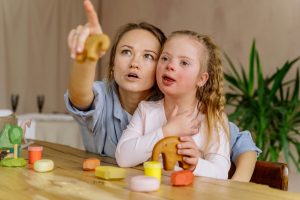 Woman and girl with Down syndrome engaging in play and learning together indoors.